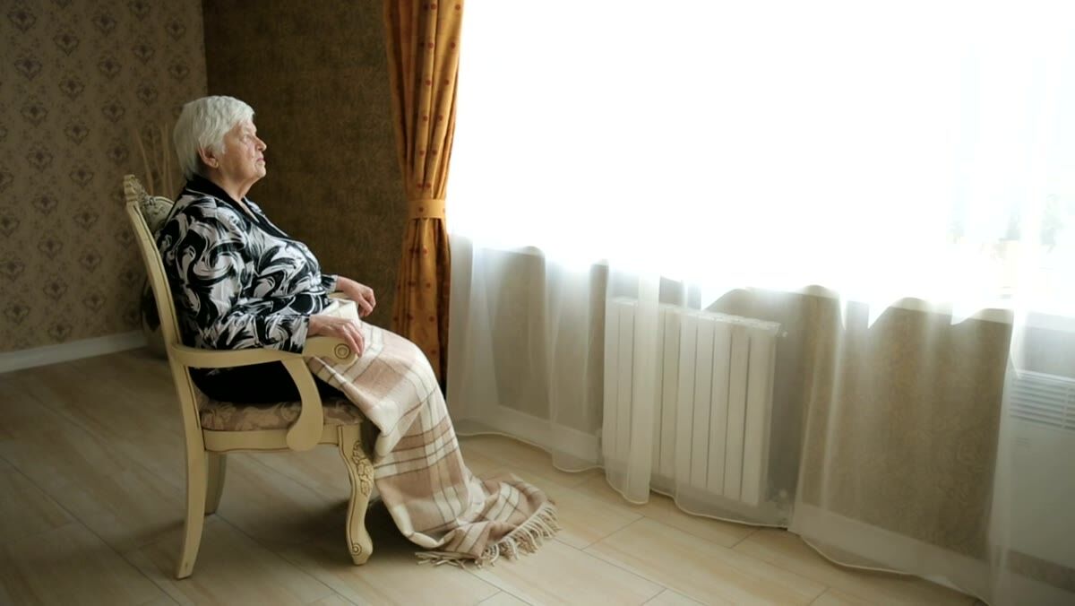 An older woman looking out of a window in warm afternoon light